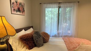 Ein ordentlich bezogenes Bett mit einer weiß-pfirsichfarbenen Steppdecke, weichen Kissen und einer Lampe auf einem Nachttisch aus Holz.