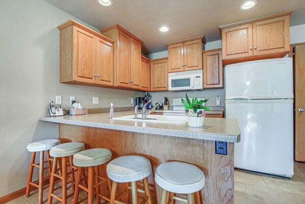A kitchen with wooden cabinets, a white refrigerator, a microwave, a sink, and bar stools.