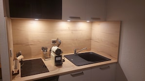 Ett kompakt kök med en svart induktionshäll, en diskho och en bänkskiva med ett förvaringsutrymme för köksredskap.