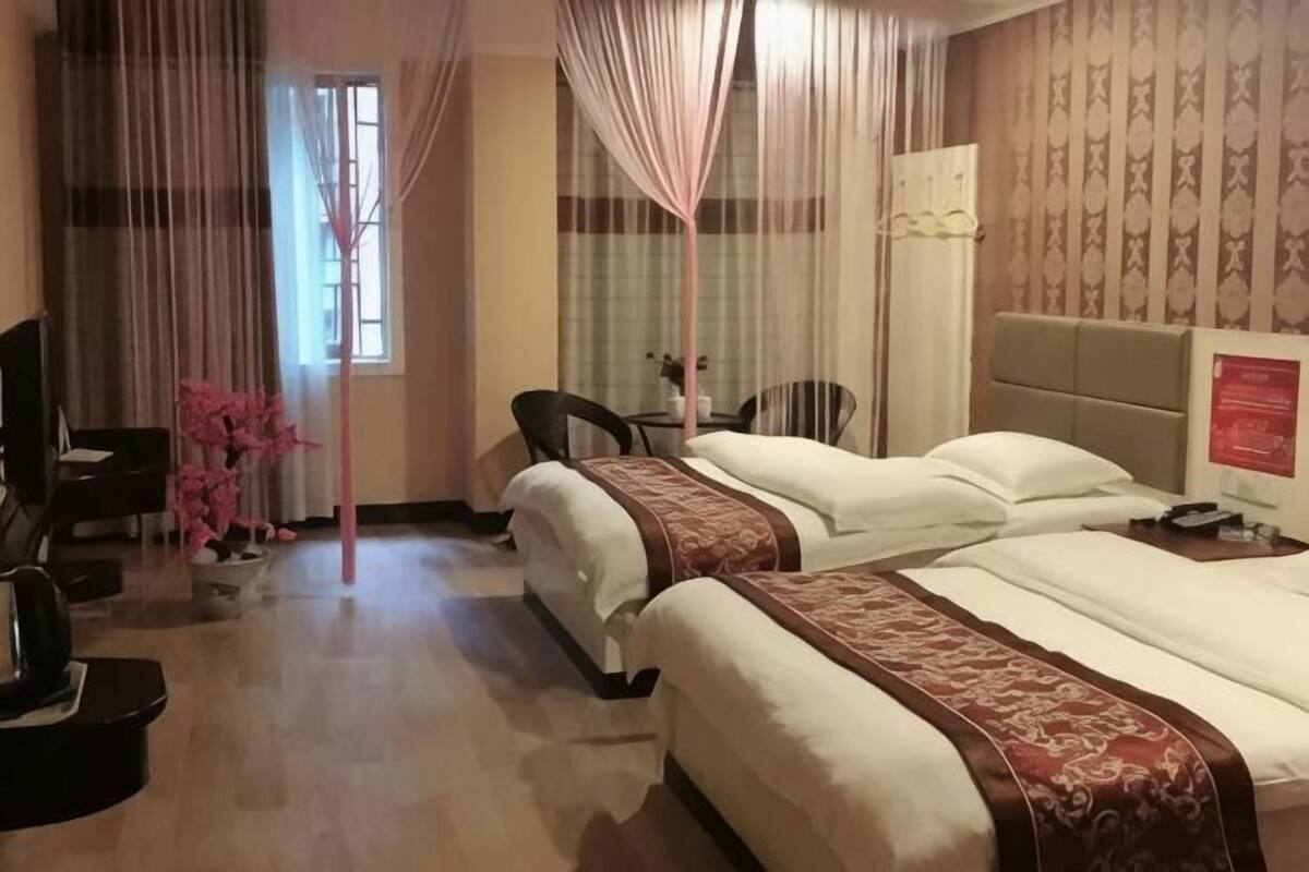 Une chambre d’hôtel avec deux lits, un bureau, une chaise, une télévision et une fenêtre avec des rideaux.