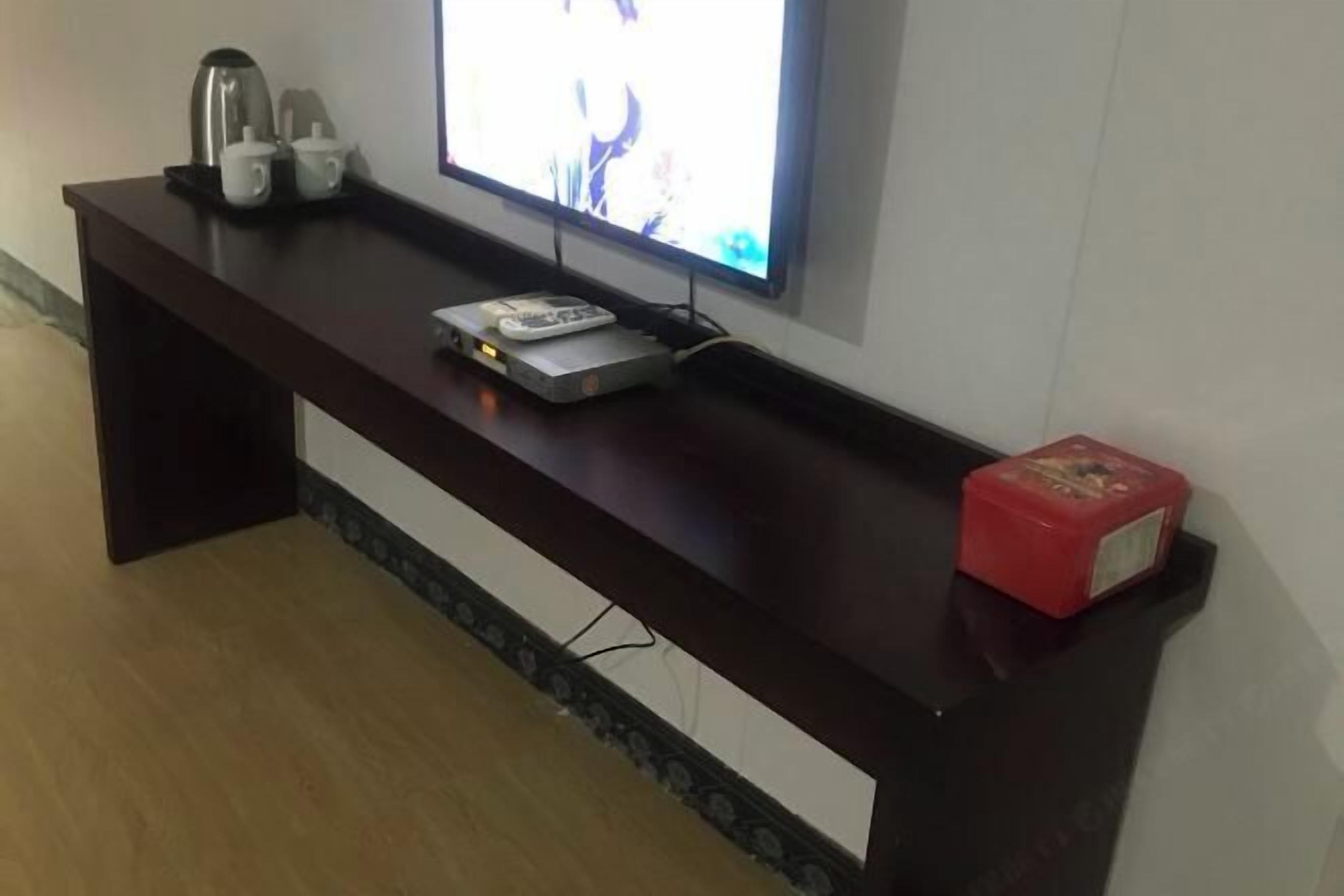 A dark wooden console table with a flat-screen TV, a remote control, and a small electronic device.
