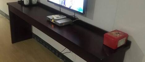 A dark wooden console table with a flat-screen TV, a remote control, and a small electronic device.