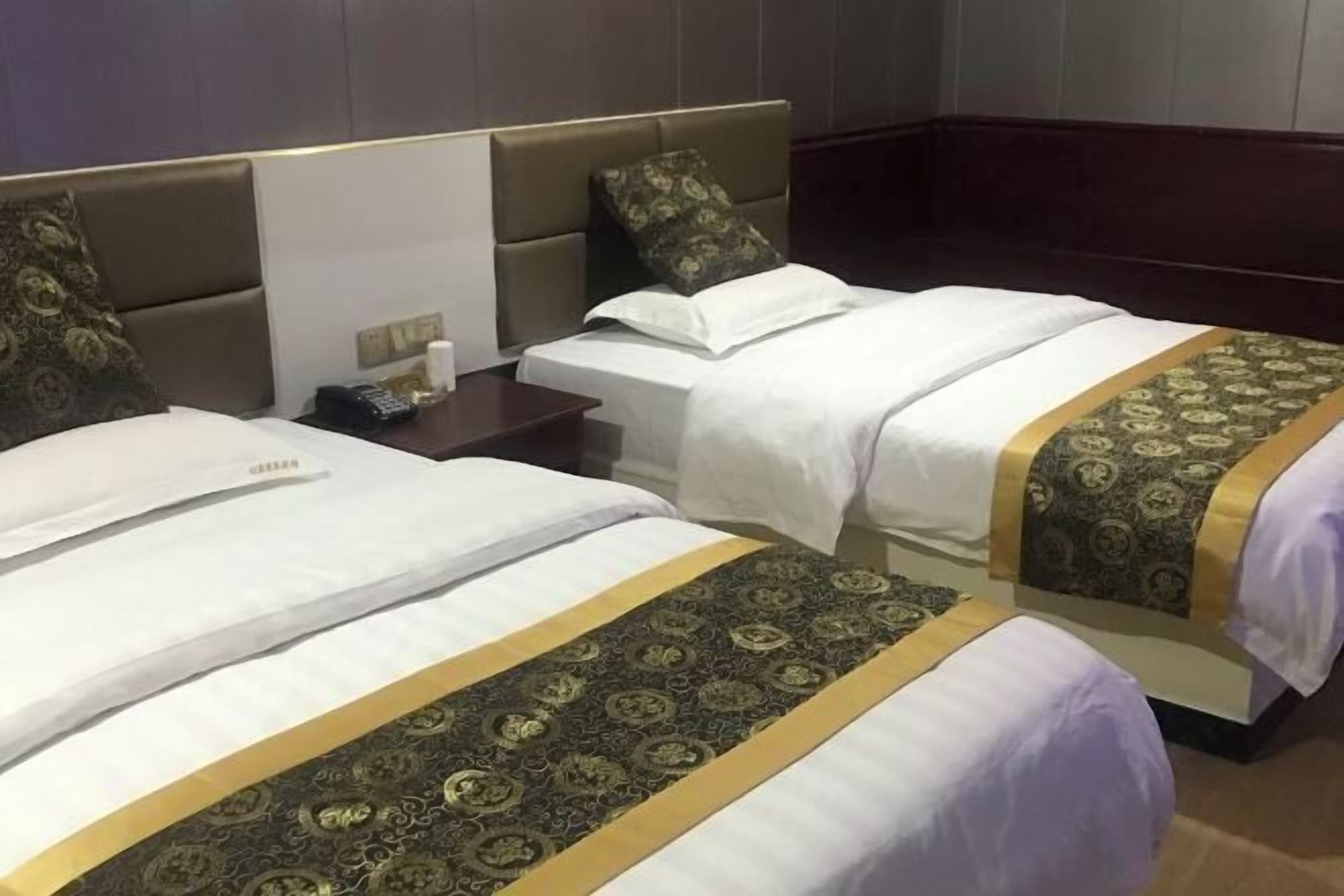 Ein Hotelzimmer mit zwei Betten, jeweils mit einem gemusterten Bettbezug und einem Kopfteil. An einem Nachttisch steht eine Lampe und ein Telefon.