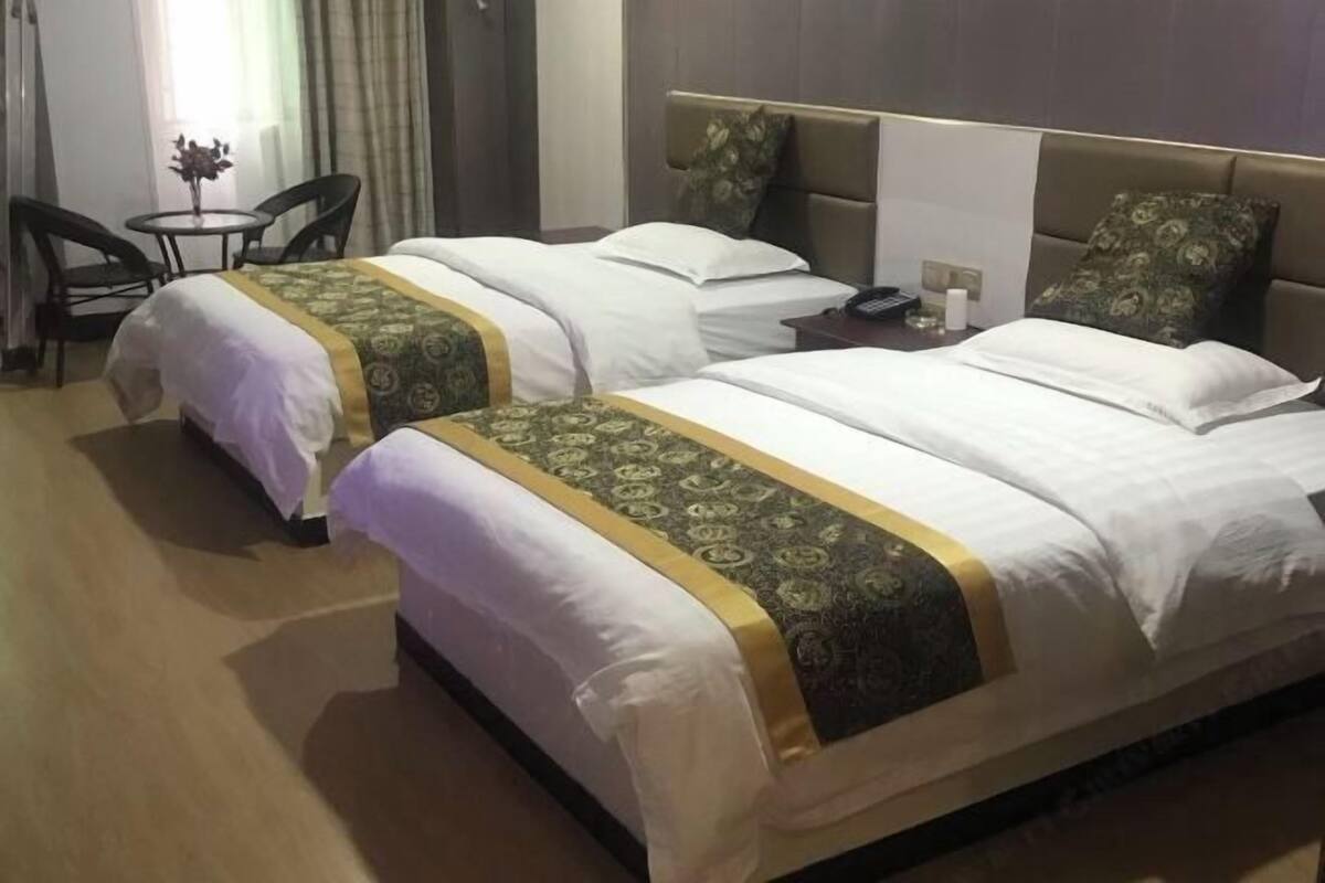 Une chambre d’hôtel avec deux lits, une petite table avec des chaises, une table de chevet avec un téléphone et une fenêtre avec des rideaux.