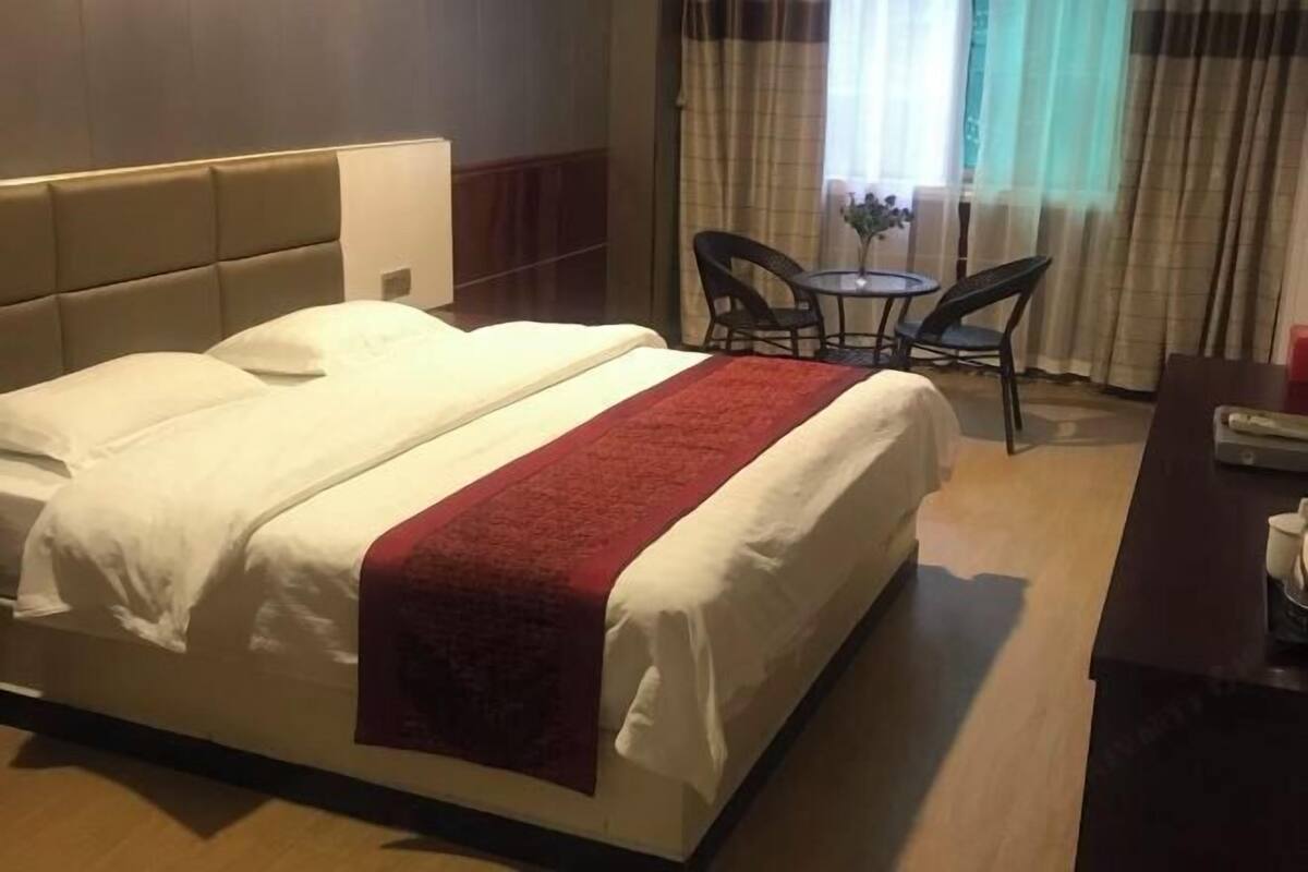 Une chambre d’hôtel avec un lit, un bureau, deux chaises, une petite table et une fenêtre avec des rideaux.