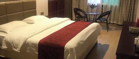 A hotel room with a bed, a desk, two chairs, a small table, and a window with curtains.