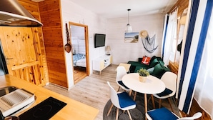 A compact living space with a kitchenette, a dining area with a round table and chairs, a green sofa, a TV, and a hanging net. - Apartment in Jaroslawiec Near the Beach (Postomino)