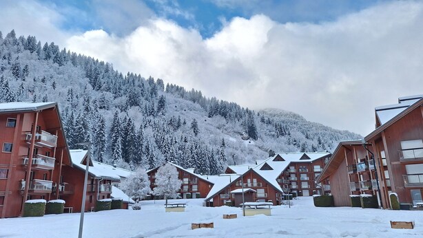 Un resort cubierto de nieve con varios edificios de madera, cada uno con balcones y una pista de esquí al fondo.