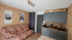 Un espacio habitable compacto con sofá, kitchenette y una pared de madera con cuadros.