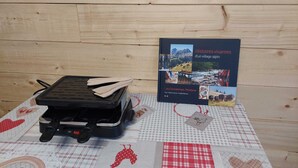 Un libro titulado 'Histoires vivantes d'un village alpin' sobre una mesa con una plancha para gofres y un mantel a cuadros.