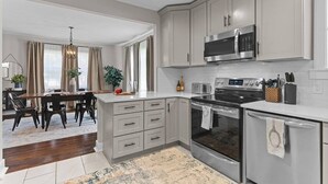 A modern kitchen with white cabinets, stainless steel appliances, and a dining area with a table and chairs. - Downtown - Sleeps 8 - We Love Doggies! (Wilmington)