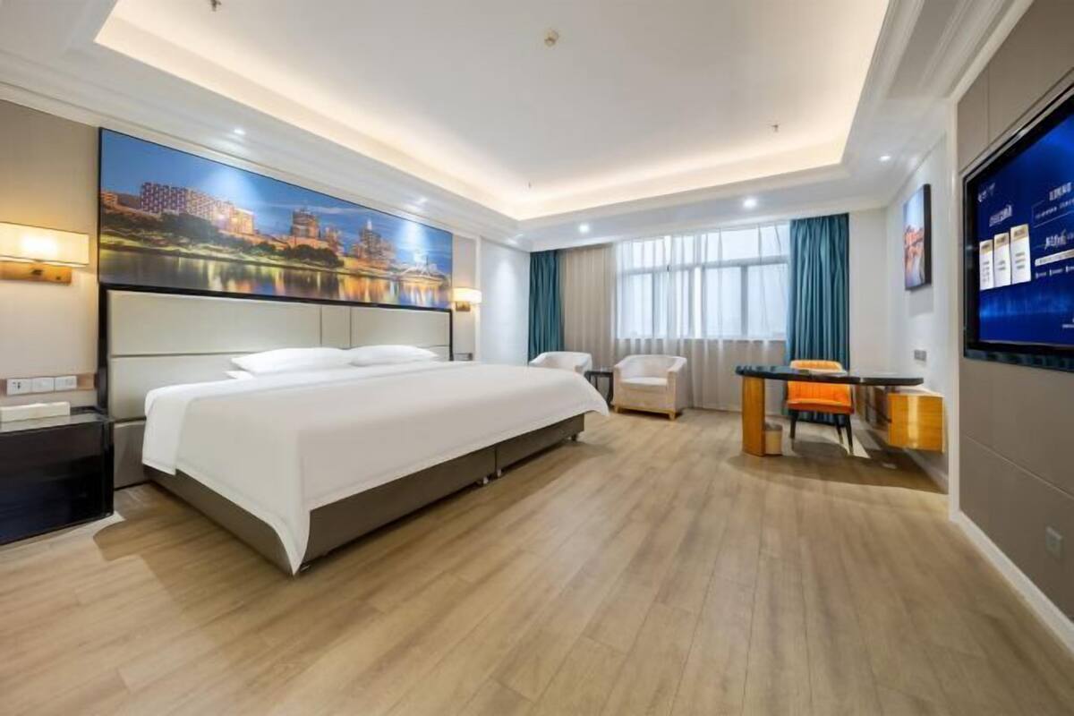 Une chambre d’hôtel avec un grand lit, un bureau avec une chaise, une télévision et un tableau au mur.