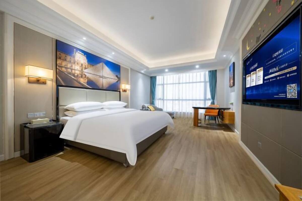 Une chambre d’hôtel équipée d’un lit, d’une table de chevet, d’un bureau, d’une chaise et d’un grand écran de télévision.