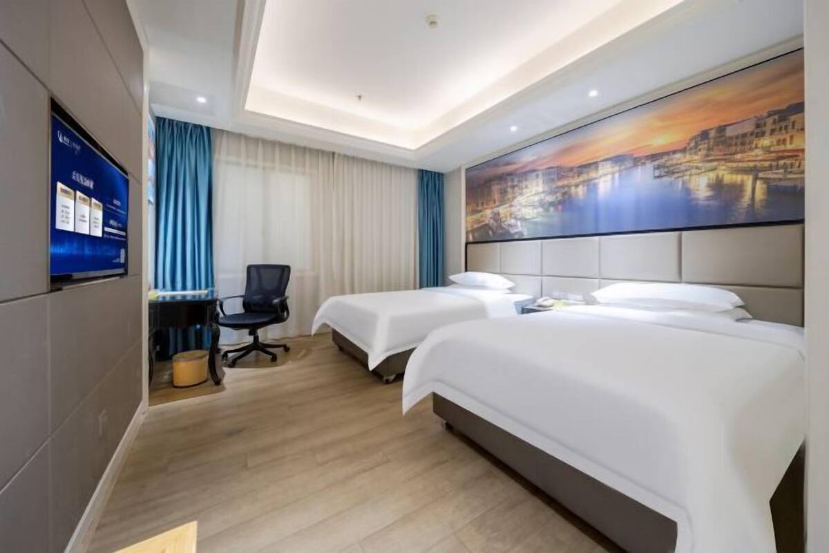 Une chambre d’hôtel avec deux lits, un bureau, une chaise, une télévision et un tableau au mur.