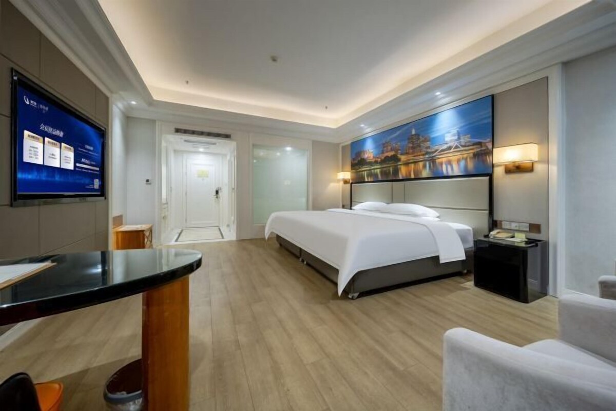 Une chambre d’hôtel avec un lit, un bureau, une télévision et un tableau au mur.