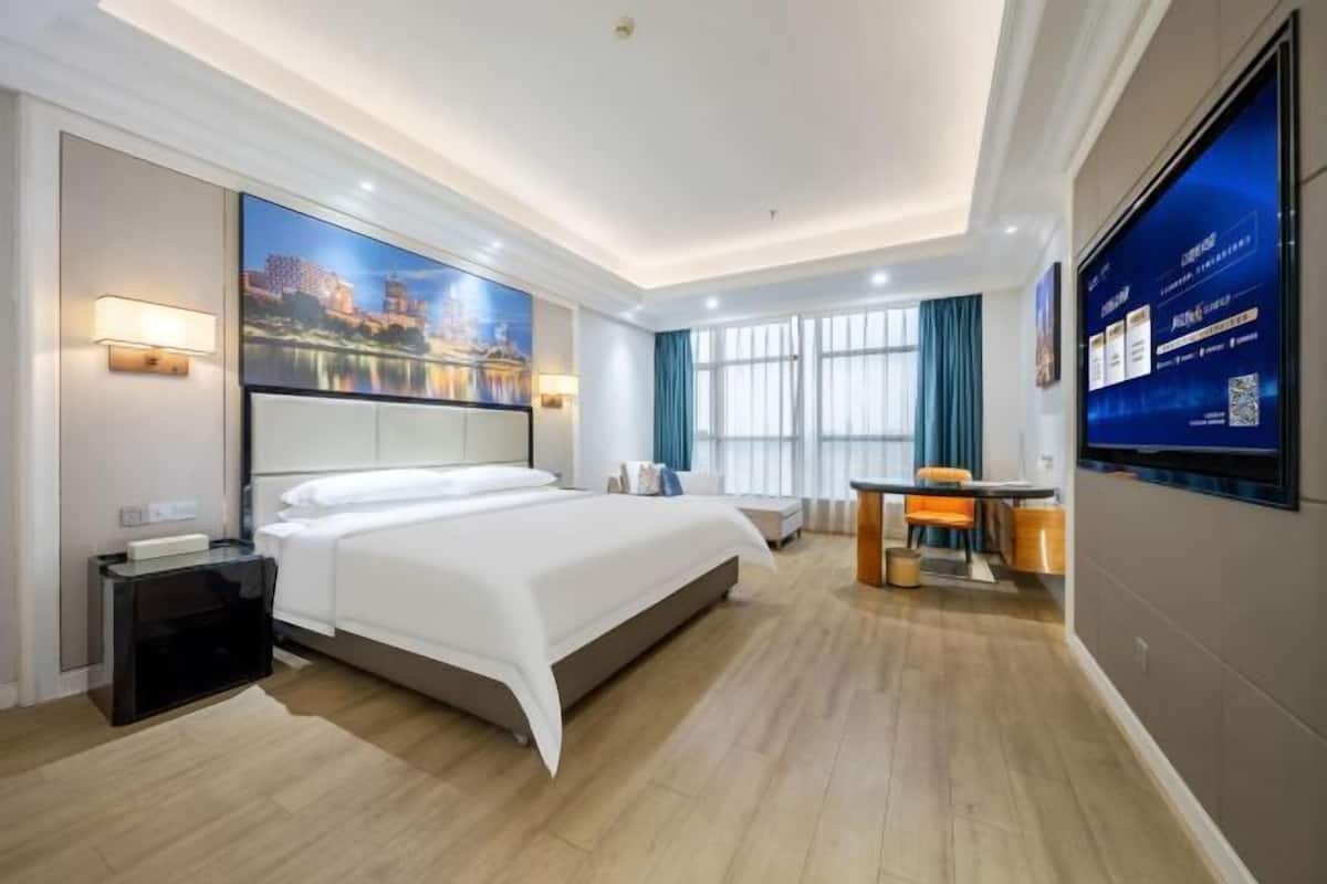 Une chambre d’hôtel avec un grand lit, un bureau, un téléviseur à écran plat et un tableau représentant un paysage urbain accroché au mur.