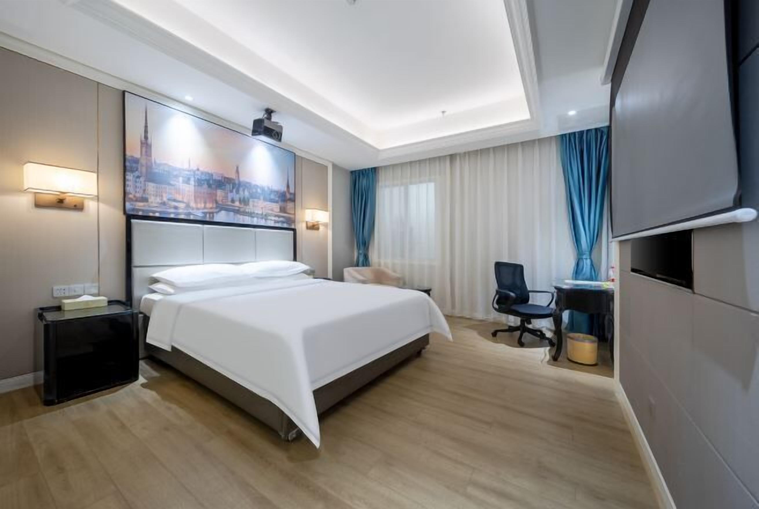 A hotel room with a bed, a desk, a chair, a television, and a painting on the wall.