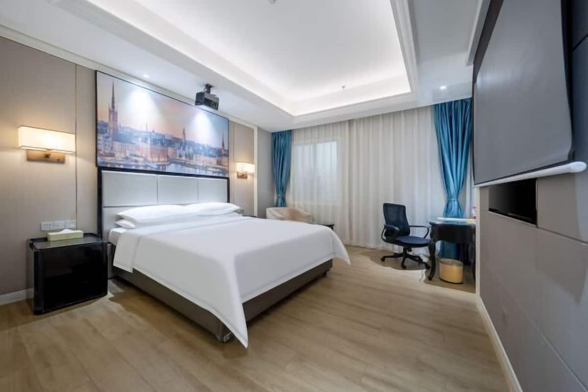 Une chambre d’hôtel avec un lit, un bureau, une chaise, une télévision et un tableau au mur.
