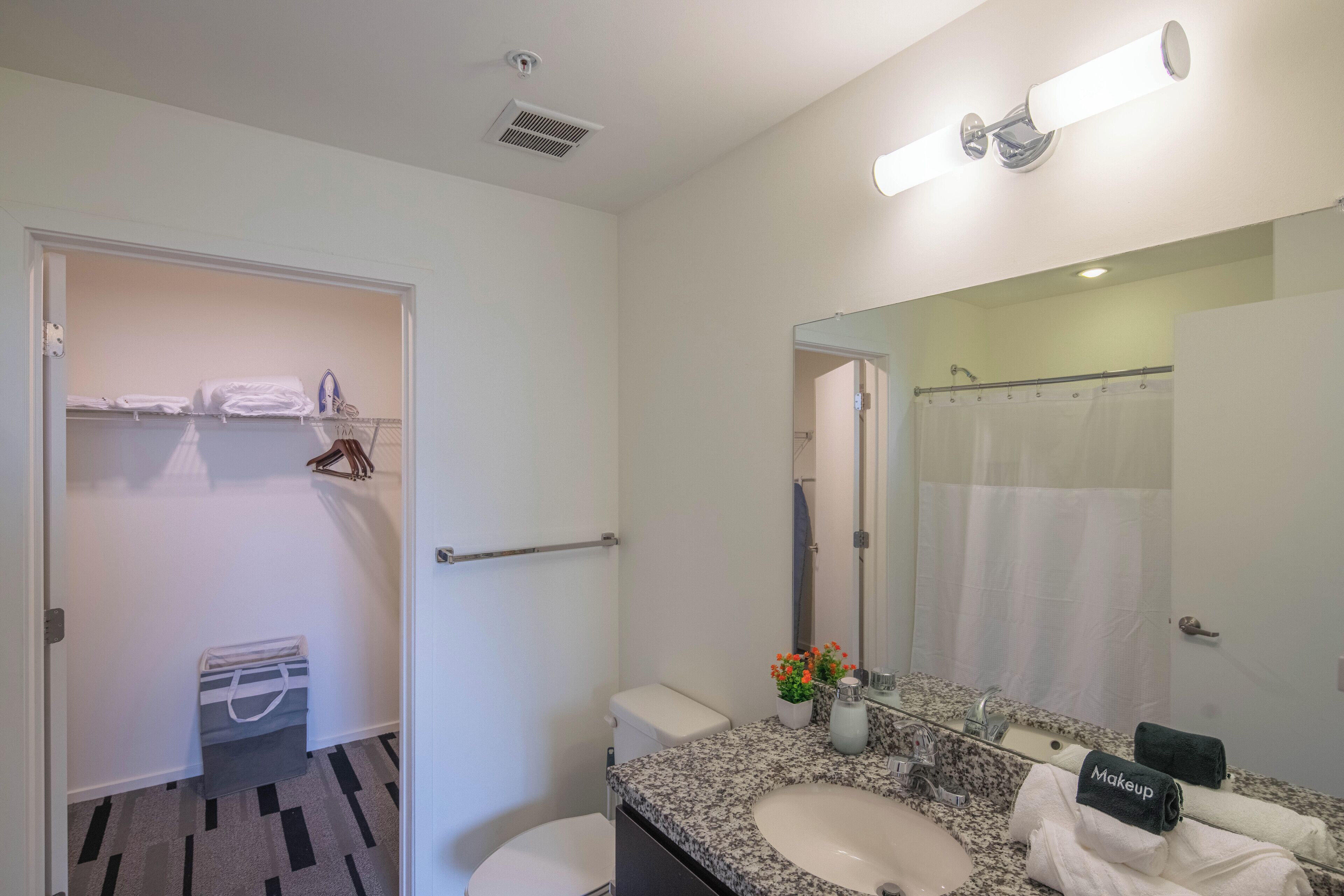 A modern bathroom with a granite countertop sink, a large mirror, a shower curtain, and a towel rack.