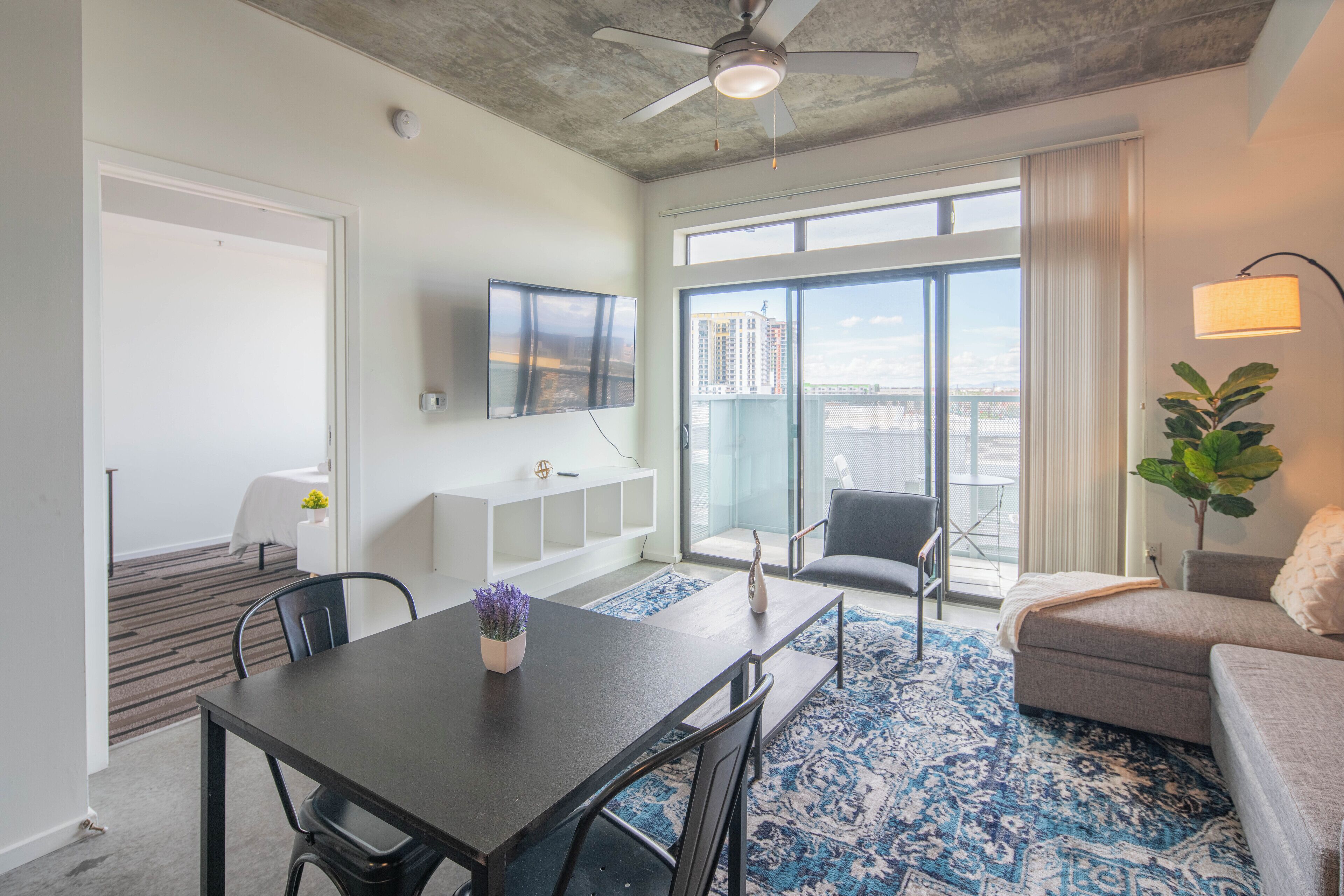 A modern living room with a dining area, large windows, and a ceiling fan.