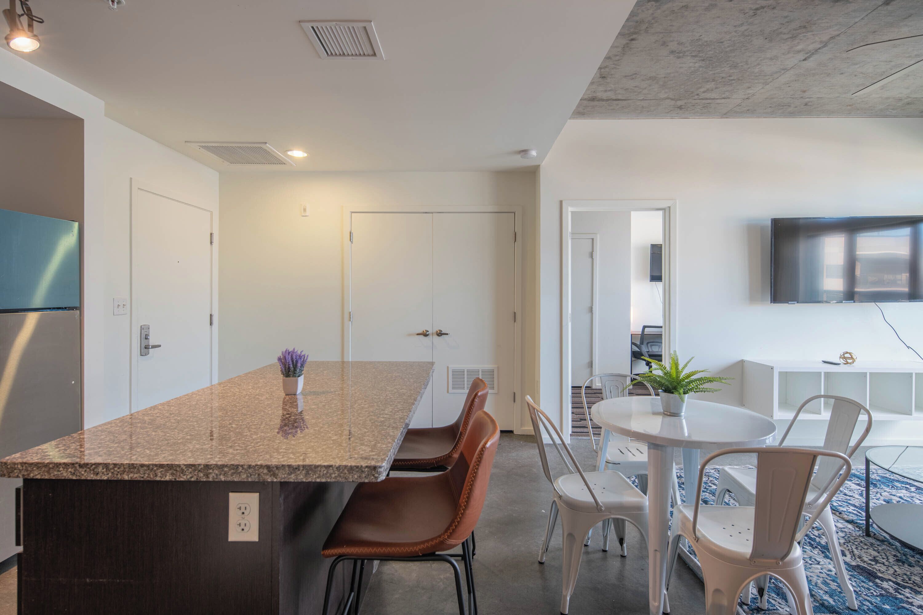 Une cuisine moderne dotée de plans de travail en granit, d’un four encastré et d’un coin repas avec des chaises blanches et une table ronde.