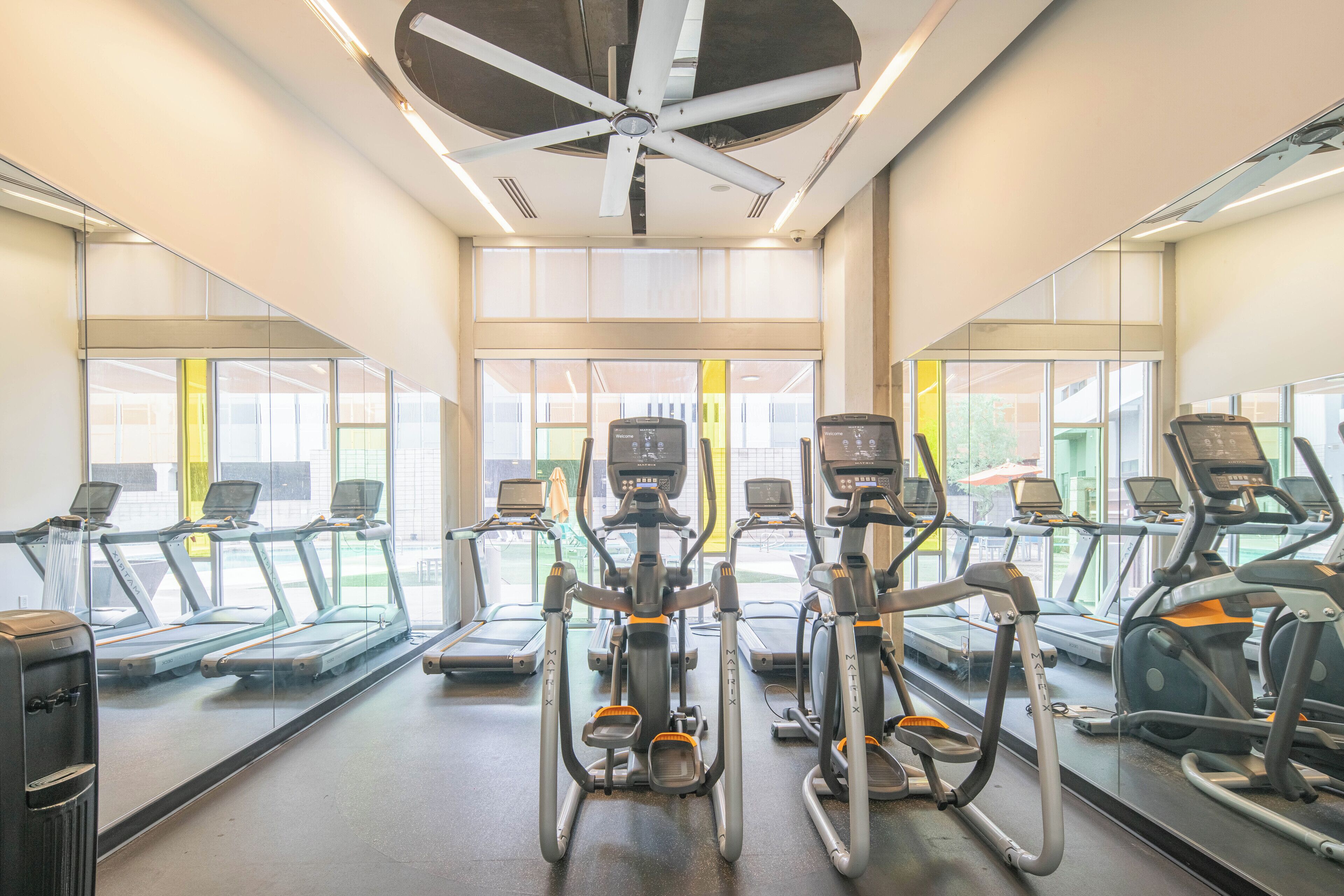 A gym with treadmills, elliptical machines, and a ceiling fan.