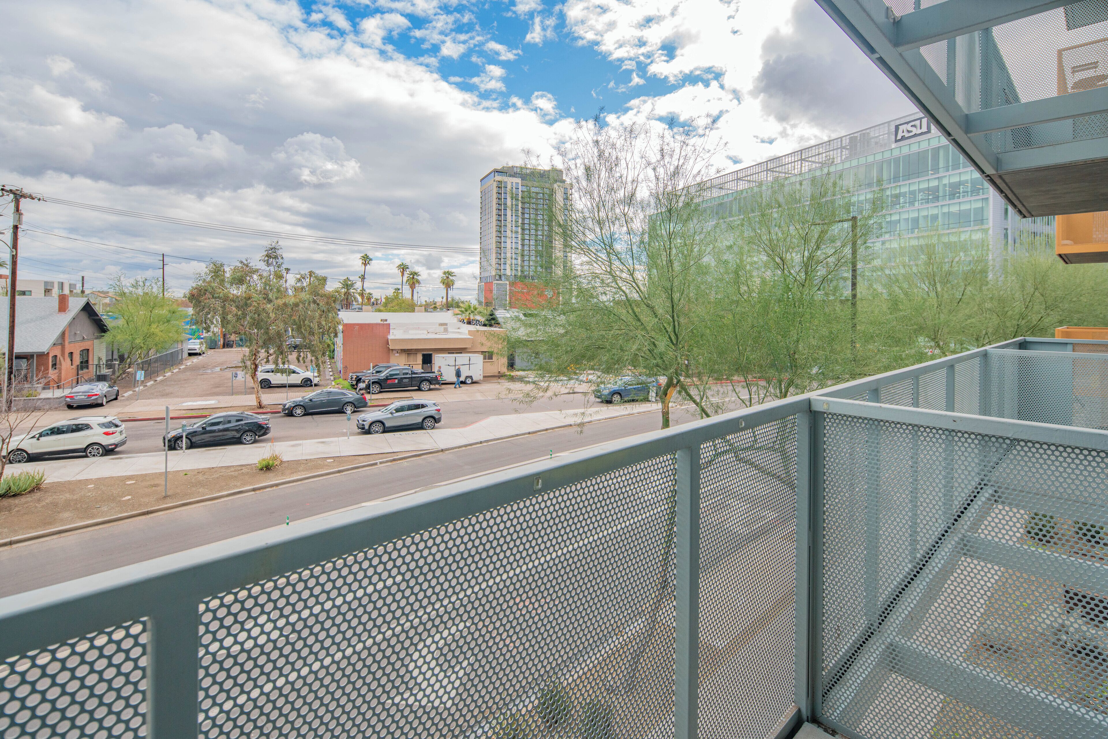 A balcony with a metal railing overlooking a street with cars and buildings.