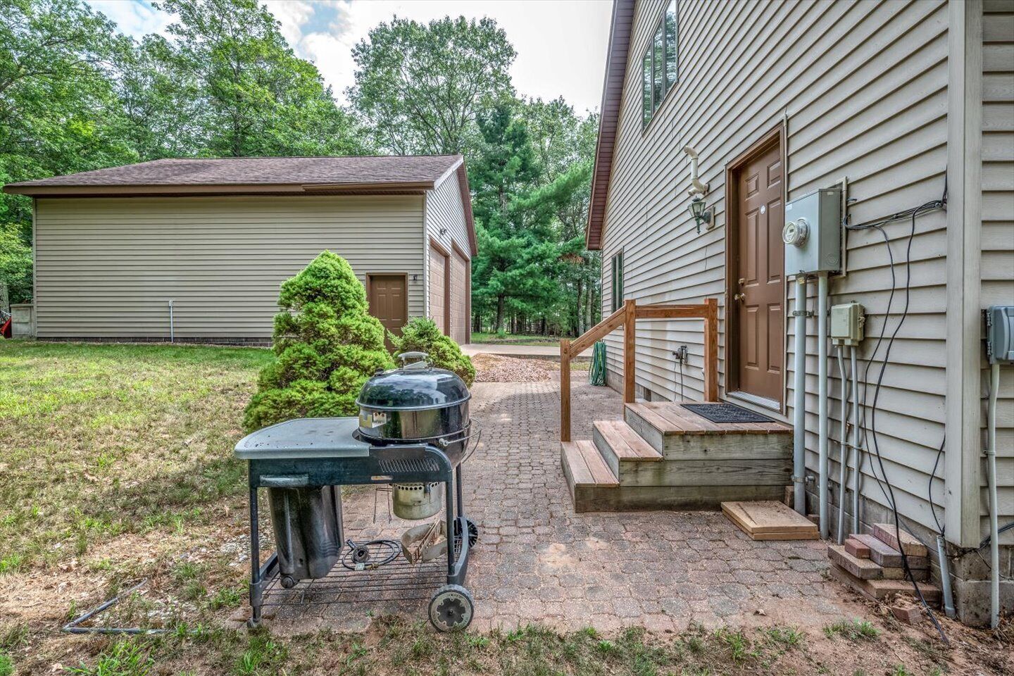 Ein Garten mit Grill, einer Holzterrasse und einem Haus mit Verkleidung und Eingangstür.