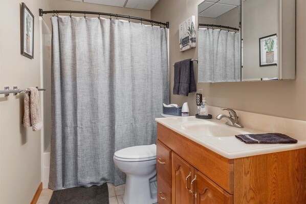 A bathroom with a shower curtain, toilet, sink, and wooden vanity.