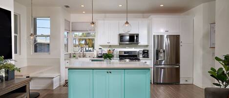 A modern kitchen with white cabinetry, a teal island, stainless steel appliances, and pendant lighting.