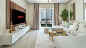 En moderne stue med et fladskærms-TV, en sofa, et sofabord og et stort vindue med gardiner.