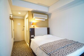 A hotel room with a bed, a headboard, an air conditioning unit, a bedside lamp, and a patterned throw blanket.