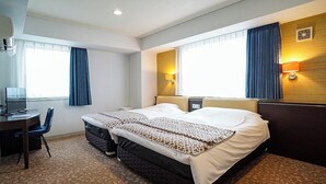 A hotel room with a bed, bedside tables, a desk with a chair, and a window with curtains.