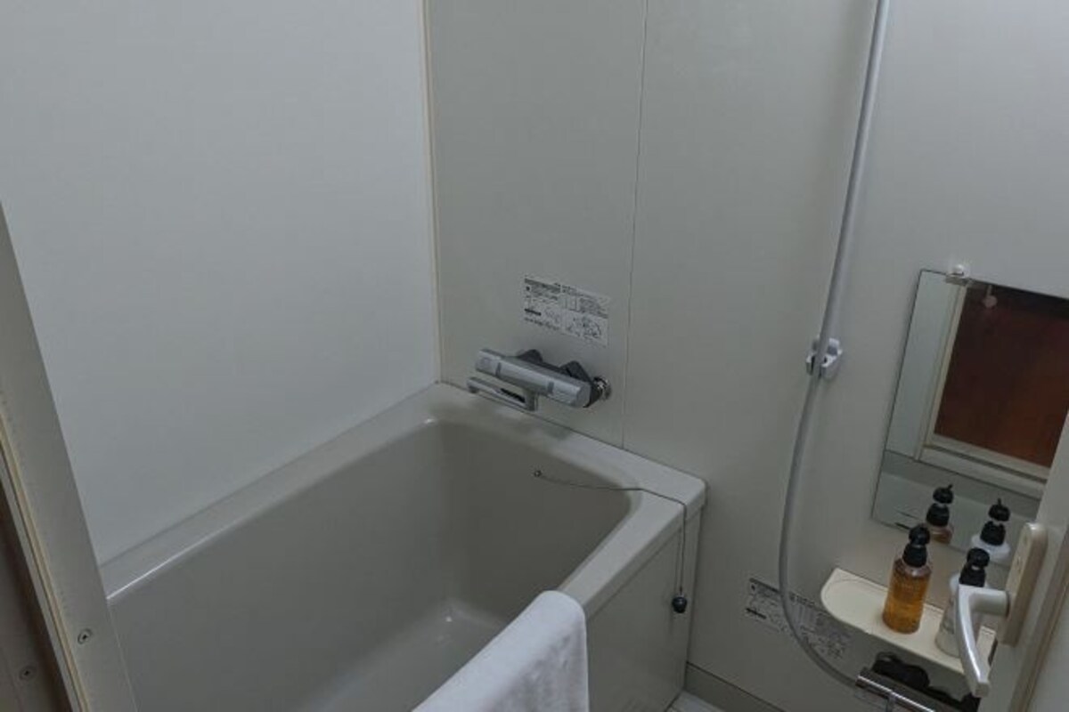 A bathroom with a bathtub, a towel, a sink with soap dispensers, and a mirror.