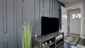 Una sala de estar moderna con un televisor de pantalla plana sobre un mueble de madera oscura, un estante pequeño con plantas y una esfera de arena decorativa.