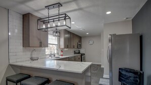 Una cocina moderna con una isla grande, taburetes de bar, un refrigerador de acero inoxidable y una lámpara colgante.