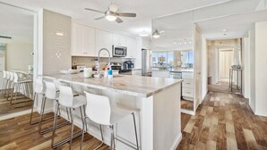 Una cocina moderna con armarios blancos, una isla grande con taburetes y un ventilador de techo.