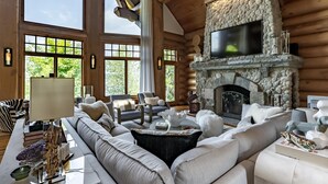 A log cabin interior with a stone fireplace, large windows, and a cozy seating area.