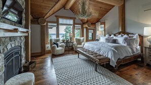 A bedroom with a stone fireplace, wooden ceiling beams, a large bed, and a view of the outdoors.