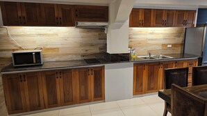 A kitchen with wooden cabinets, a microwave, and a stainless steel sink. - Beach Penthouse (Island  Samal, Davao Region)