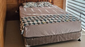 A bedroom with a wooden headboard, a bed with a patterned bedspread, and a window with blinds. - Beach Penthouse (Island  Samal, Davao Region)