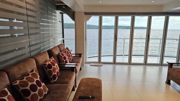 A modern living room with a large sliding glass door leading to a balcony with a view of a body of water. - Beach Penthouse (Island  Samal, Davao Region)