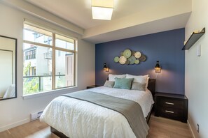 A bedroom with a large bed, bedside tables, a window with a view, and decorative wall art. - Sun-Drenched Sophistication (Victoria North)