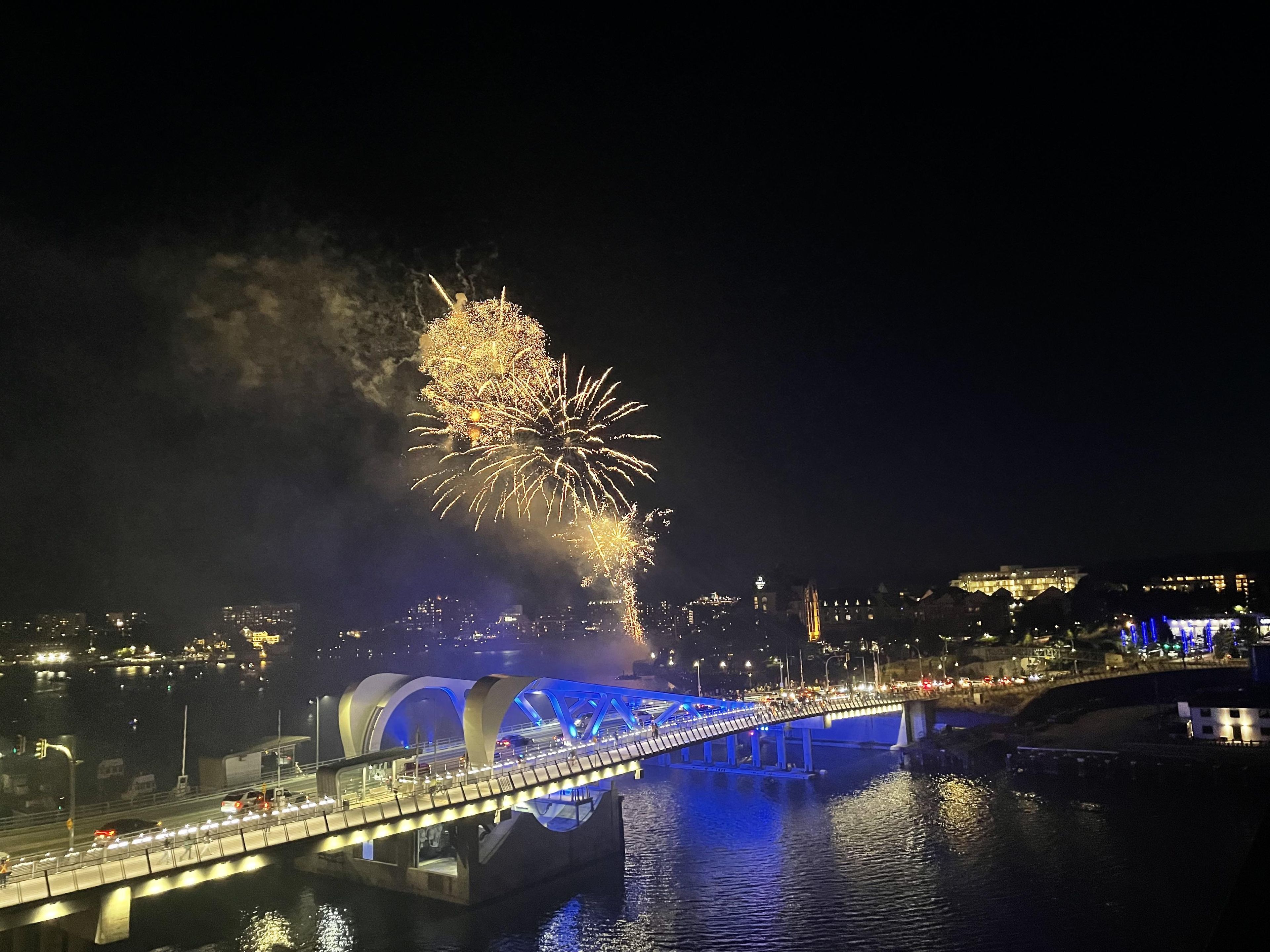 A nighttime view of a bridge with fireworks in the background.