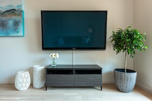 A modern living room with a flat-screen TV mounted on the wall, a grey entertainment unit, a potted plant, and two decorative vases. - Sun-Drenched Sophistication (Victoria North)
