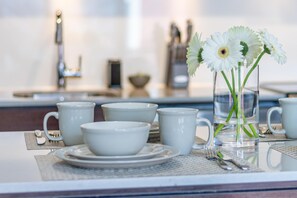 A breakfast setting with white cups, saucers, and a clear glass vase with flowers on a table. - Sun-Drenched Sophistication (Victoria North)