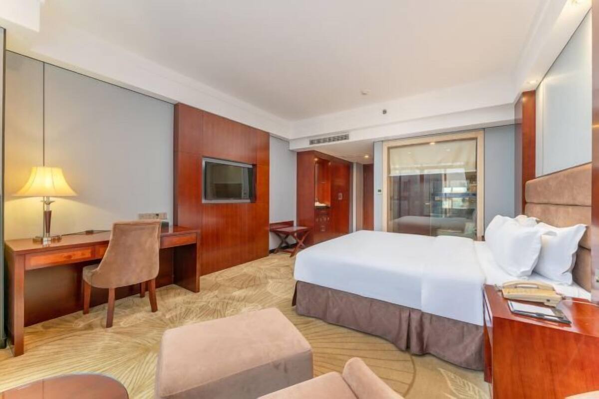 A hotel room with a bed, desk, chair, and TV.