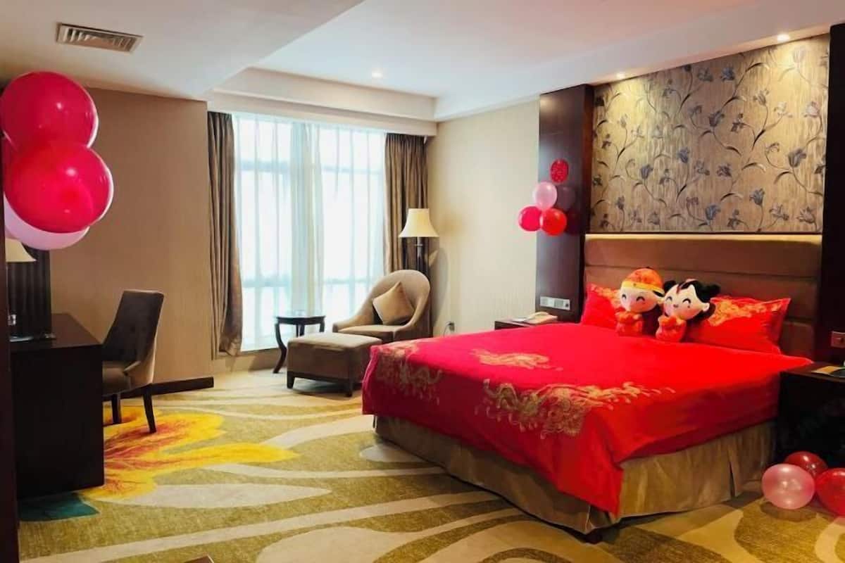 A hotel room with a large bed, a desk, a chair, and a window with curtains.