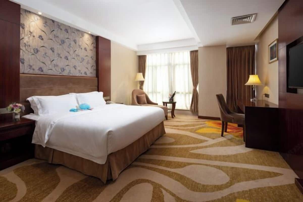 A hotel room with a large bed, a desk, a chair, a television, and a patterned wall.