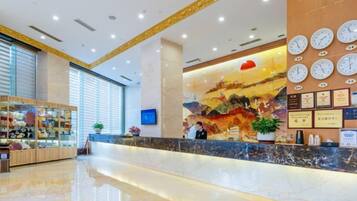 A hotel reception area with a marble counter, a large wall clock, and a mural.